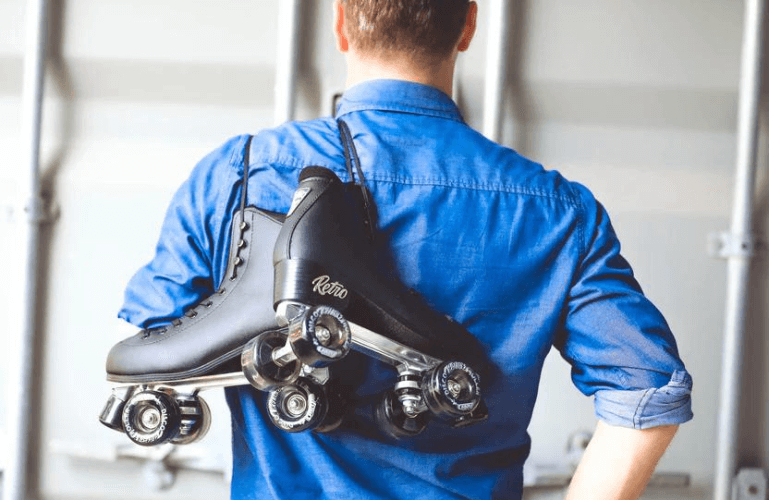 man with denim blue shirt and black retro skates over shoulder