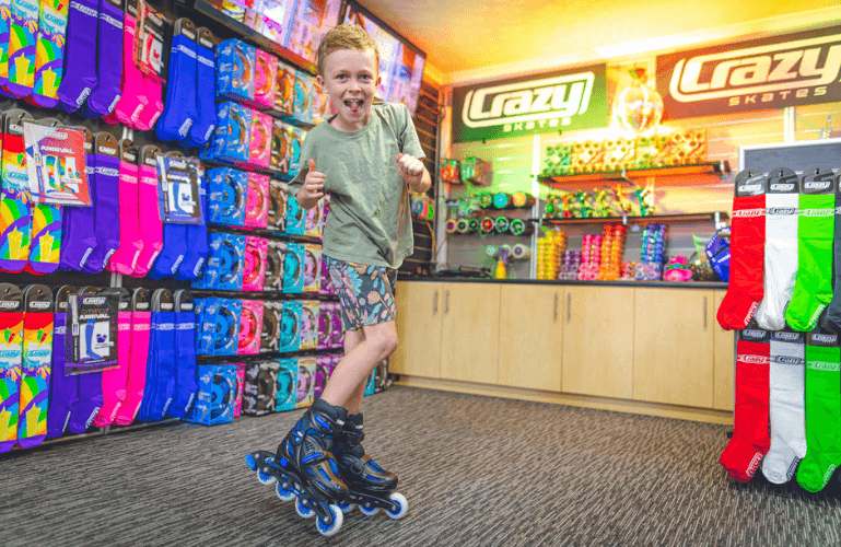 ecstatic boy in crazy skates store wearing black and blue inline skates